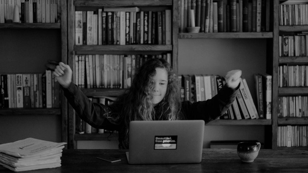tjej sitter framför datorn med händerna i luften