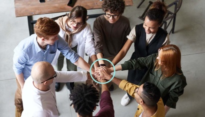 Kollegor och medarbetare står i en ring och samlar sina händer för att symbolisera teamwork och ett framgångsrikt sätt att mäta medarbetares upplevelse