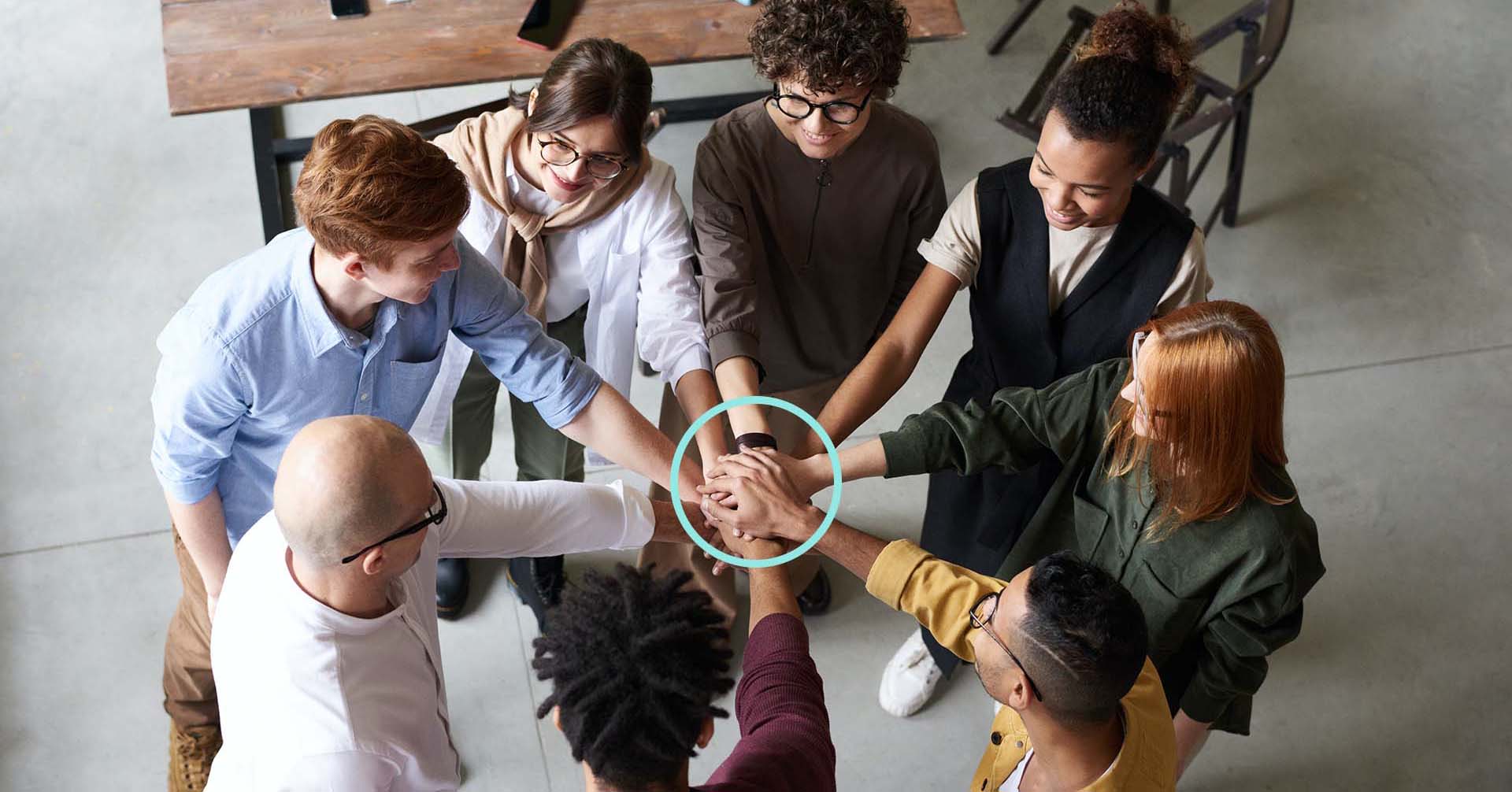 Kollegor och medarbetare står i en ring och samlar sina händer för att symbolisera teamwork och ett framgångsrikt sätt att mäta medarbetares upplevelse