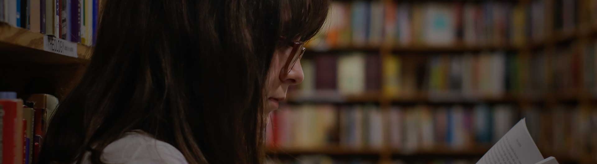 tjej sitter i ett skolbibliotek och läser en bok för att skildra skolundersökning